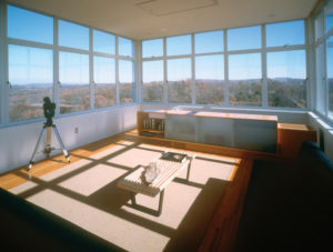 Modern living room surrounded by large full windows looking out to the forest on every side