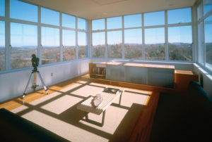 Modern living room surrounded by large full windows looking out to the forest on every side