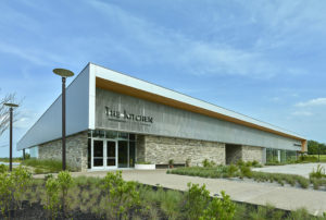 Metal and stone exterior face with walkways and landscaping facing the parking area