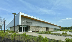 Metal and stone exterior face with walkways and landscaping facing the parking area