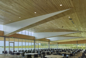 Dining room interior below stark white frames lifting wooden slat ceilings overlooking the lake water through glass