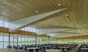 Dining room interior below stark white frames lifting wooden slat ceilings overlooking the lake water through glass