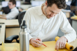 Ryan Camp wearing a white shirt marking on tracing paper with a red pen