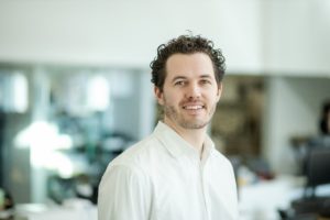 MBA team member headshot featuring Ryan Camp with curly dark hair wearing a white shirt while smiling