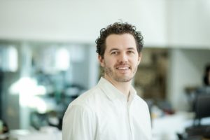 MBA team member headshot featuring Ryan Camp with curly dark hair wearing a white shirt while smiling