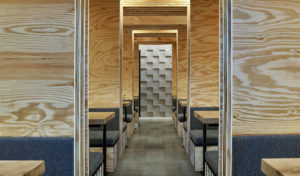 A well-lit hallway with wooden plywood booths on either side