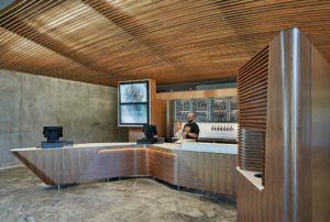 A restaurant worker at the checkout register surrounded in a room of concrete and wood overlooking the dining room