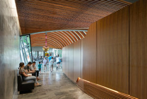 A shot of a hallway, one wall is concrete the other is wood below a beautiful wooden slat ceiling