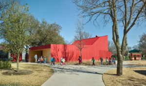 Lamplighter Barn's red exterior with children rushing to school in a line leading towards a wooden opening entrance to the structure