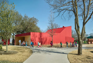 Lamplighter Barn's red exterior with children rushing to school in a line leading towards a wooden opening entrance to the structure