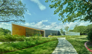 A stark wood and metal profile shot of the exterior structure with walking paths and lush landscaped greenery