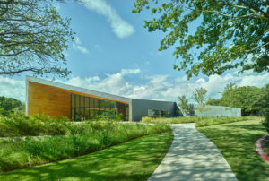 A stark wood and metal profile shot of the exterior structure with walking paths and lush landscaped greenery