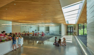 Lamplighter Innovation Lab building shows glass concrete and wooden ceilings in a modern space above young children working on art projects