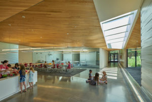 Lamplighter Innovation Lab building shows glass concrete and wooden ceilings in a modern space above young children working on art projects
