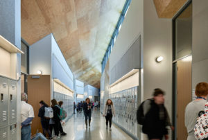 Thaden Reels school hallways featuring bright steel lockers and a steep ceiling above students rushing hurriedly to class