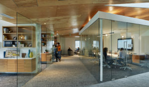 Glass interior rooms showing modern office spaces and a carpeted hallway with modern wooden ceiling cut at an angle