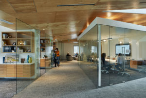 Glass interior rooms showing modern office spaces and a carpeted hallway with modern wooden ceiling cut at an angle