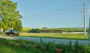 Thaden Reels exterior photo of an angular green building seen from across a grassy field as a car drives by