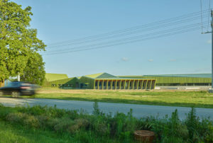 Thaden Reels exterior photo of an angular green building seen from across a grassy field as a car drives by