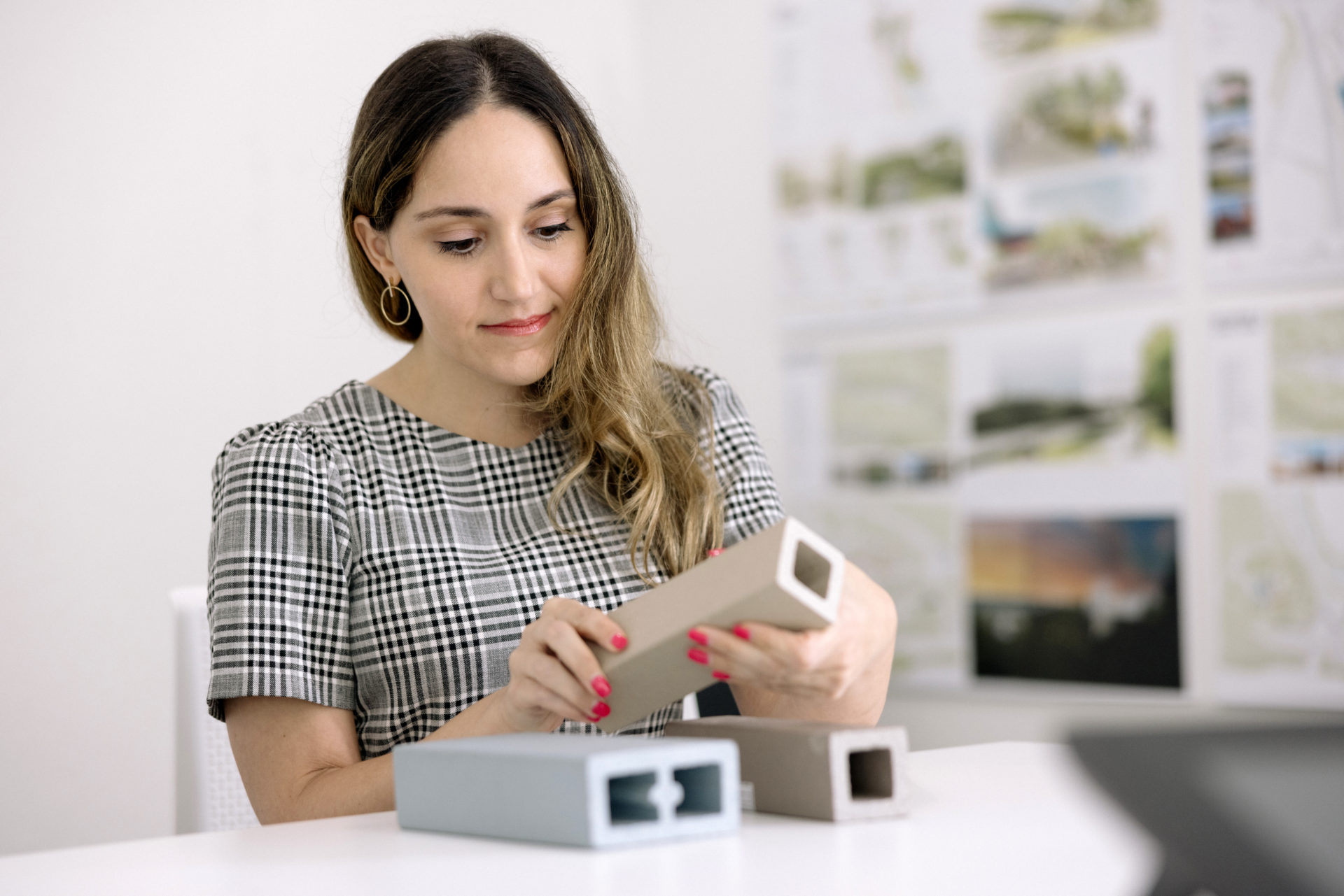 A female architect with dark hair with blonde highlights wearing a modern checkered dress working with models in a white office