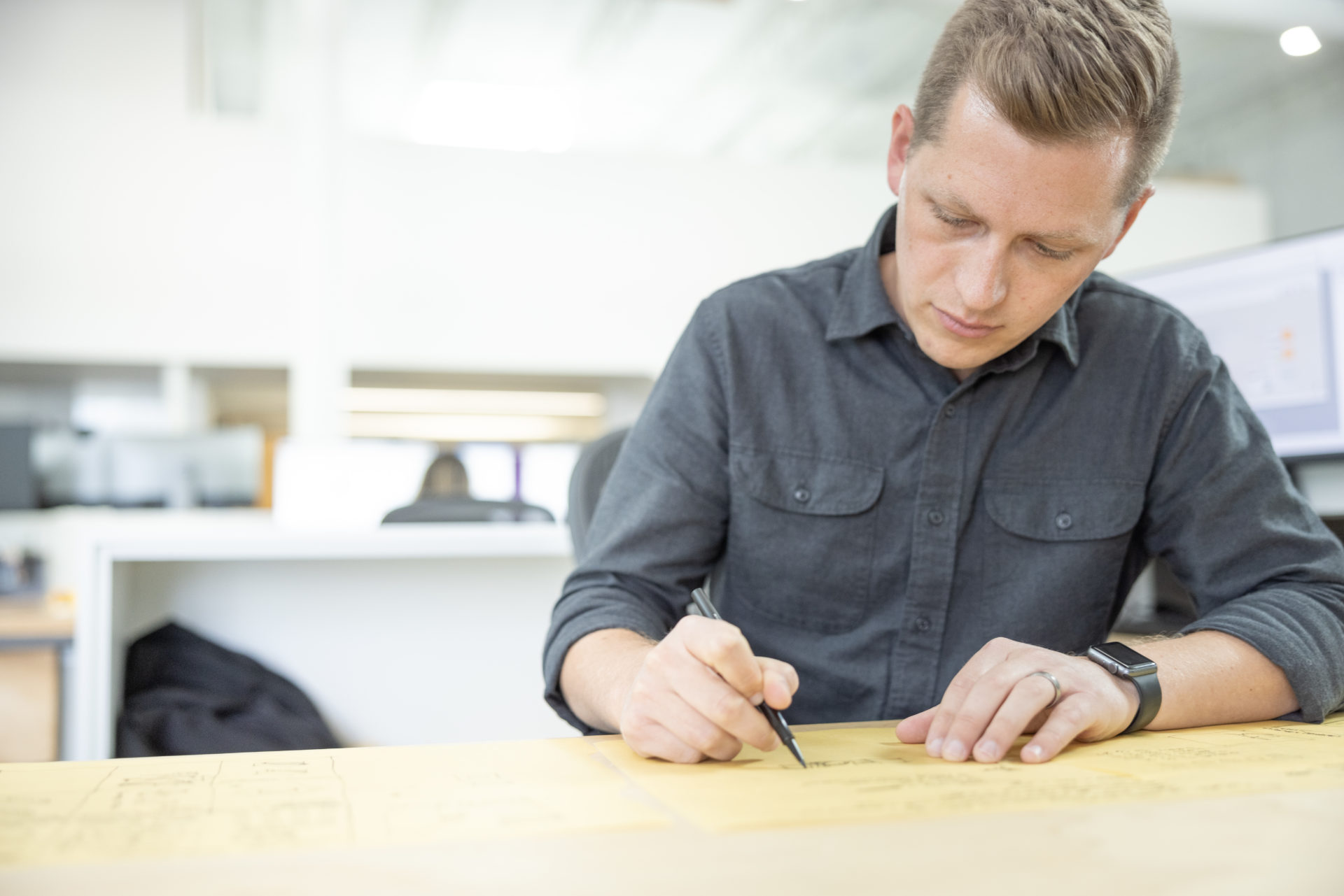 A team member wearing a cool-gray button-up shirt drawing with a pencil on plans