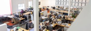 Overhead view of a bustling office with architects working at wooden desks in a white room